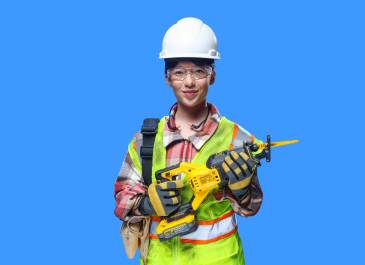Woman wearing hard hat, safety glasses, hi-visibility vest, and safety gloves holding a power tool smiling at camera.