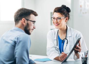 Female doctor seated across from male patient shows clipboard with treatment plan.