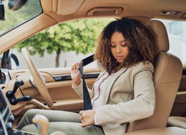 Woman sitting in the driver's seat buckling seat belt.