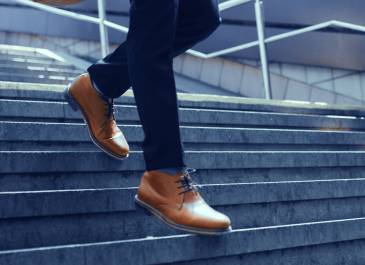 Man wearing brown shoes walking down the stairs. Image cropped to focus on lower legs and shoes.