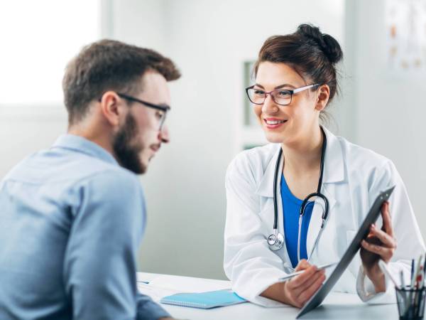 Female doctor seated across from male patient shows clipboard with treatment plan.