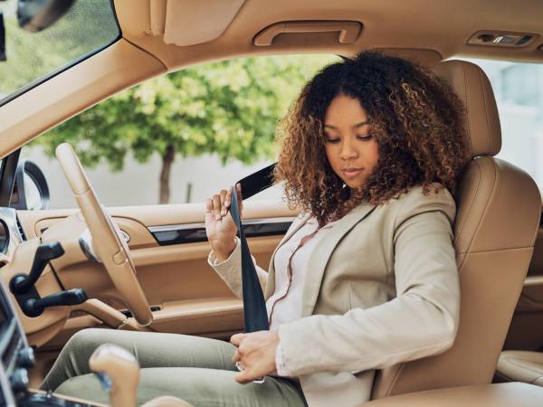 Woman sitting in the driver's seat buckling seat belt.