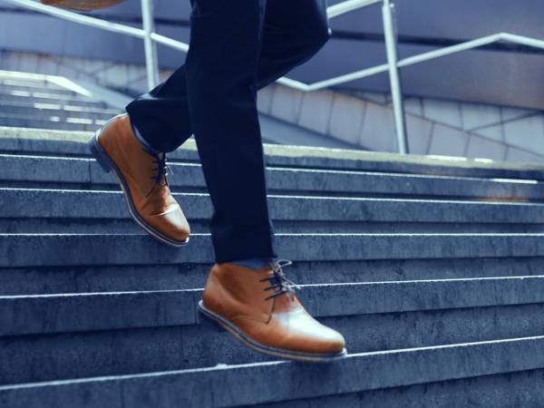 Man wearing brown shoes walking down the stairs. Image cropped to focus on lower legs and shoes.