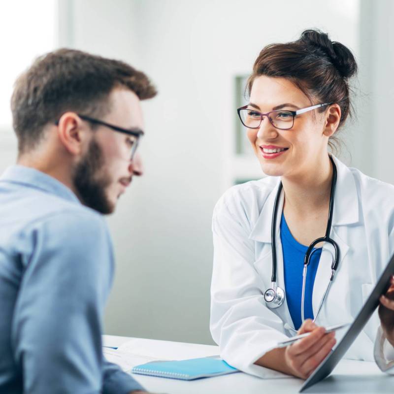 Female doctor seated across from male patient shows clipboard with treatment plan.