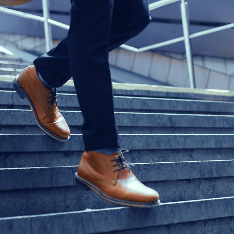 Man wearing brown shoes walking down the stairs. Image cropped to focus on lower legs and shoes.
