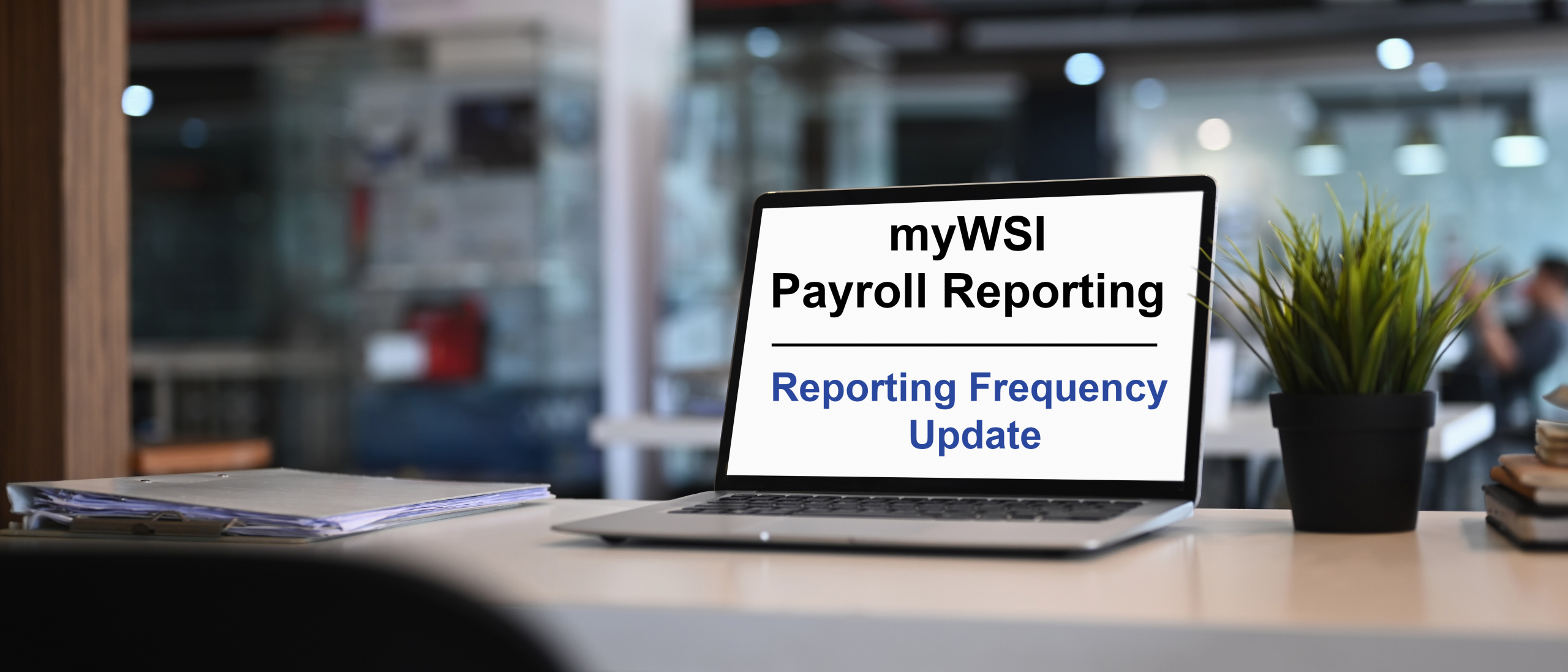 Laptop computer in softly lit office displaying the text "myWSI Payroll Reporting - Reporting Frequency Update