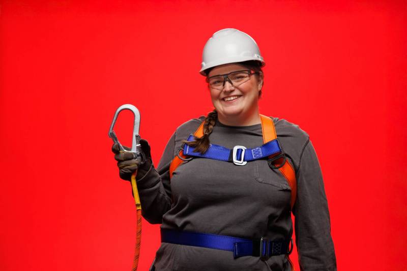 Woman wearing safety harness, hard hat, and safety glasses smiles at the camera