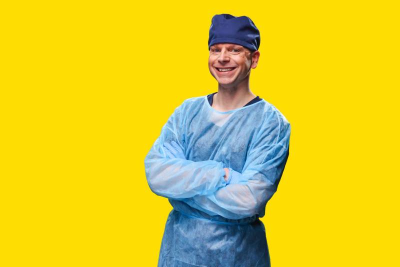 Man wearing scrubs smiling with arms folded across chest.