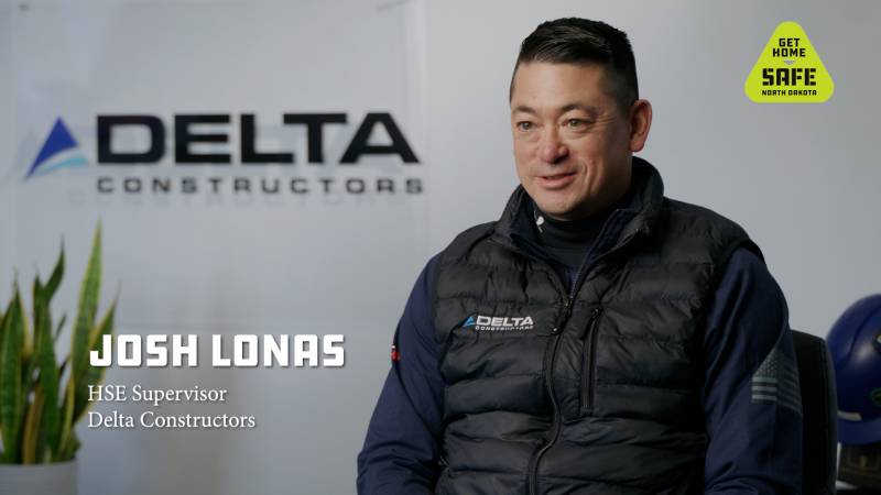 Man in Delta Constructors vest sitting with Delta Constructors name on the background and the Get Home Safe logo in the upper right hand corner
